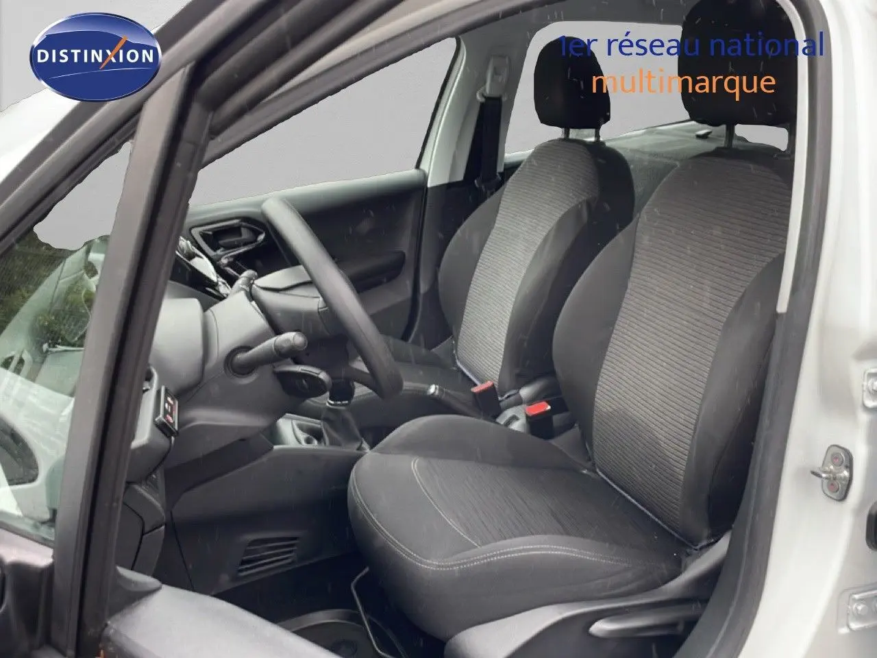 Vue intérieure côté conducteur de la Peugeot 208 Société blanche, montrant les sièges tissu noirs et le volant.