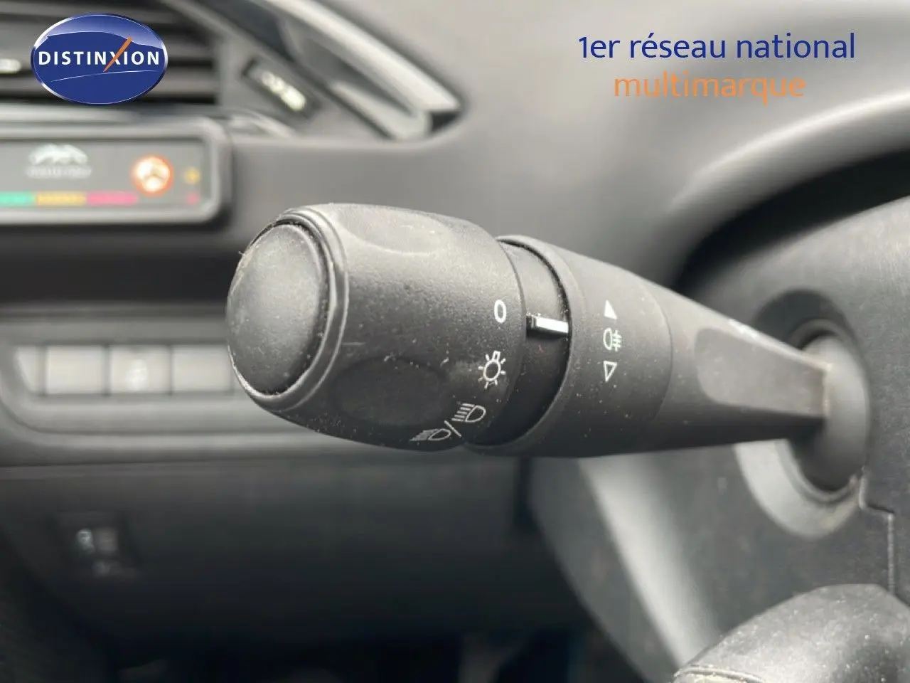 Gros plan sur la commande des phares à gauche du volant dans l’habitacle sombre d’une Peugeot 208 Blanc Banquise.