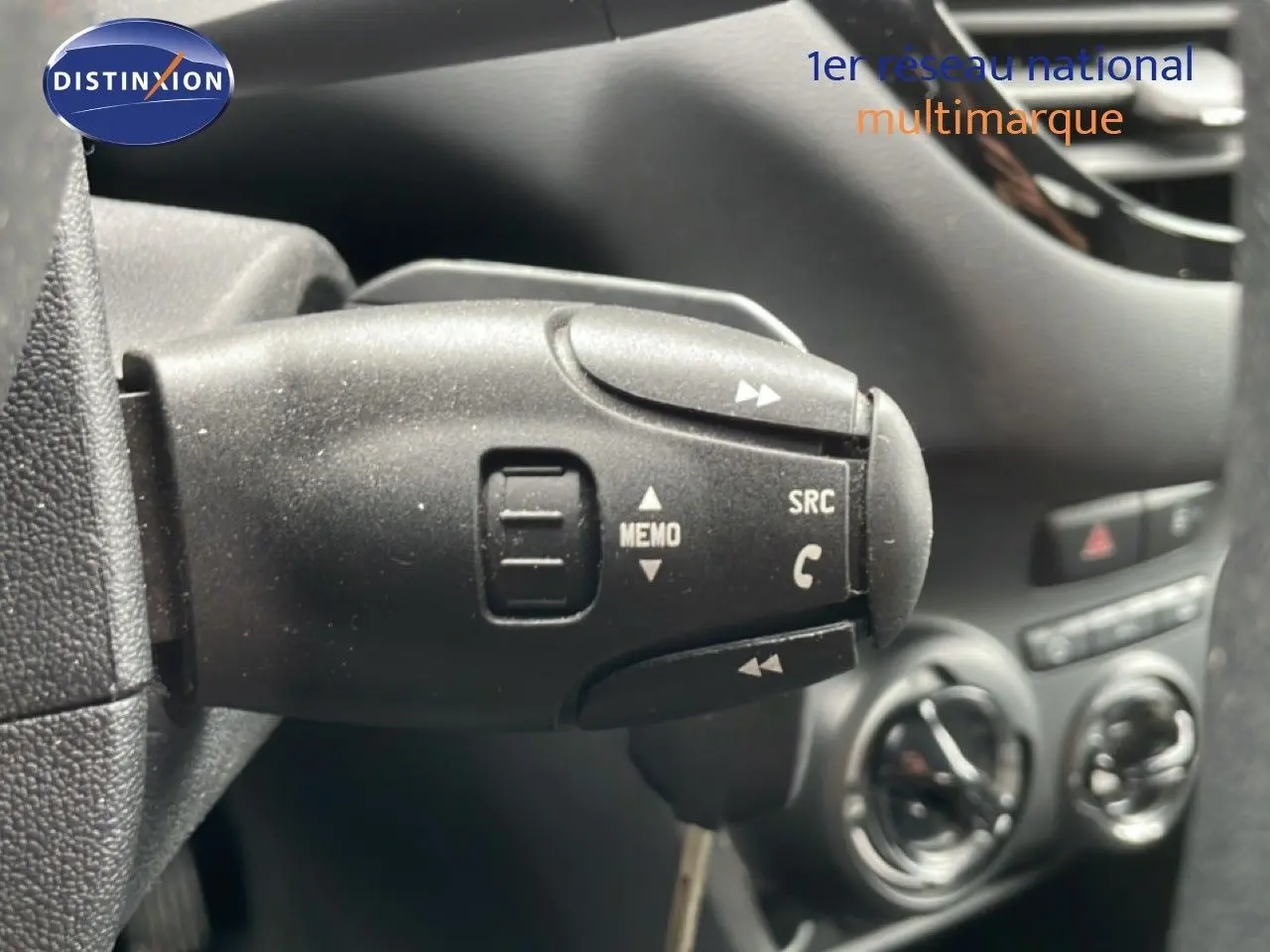 Gros plan sur la commande au volant de la Peugeot 208 Société blanche, avec tableau de bord et aérateurs en arrière-plan.