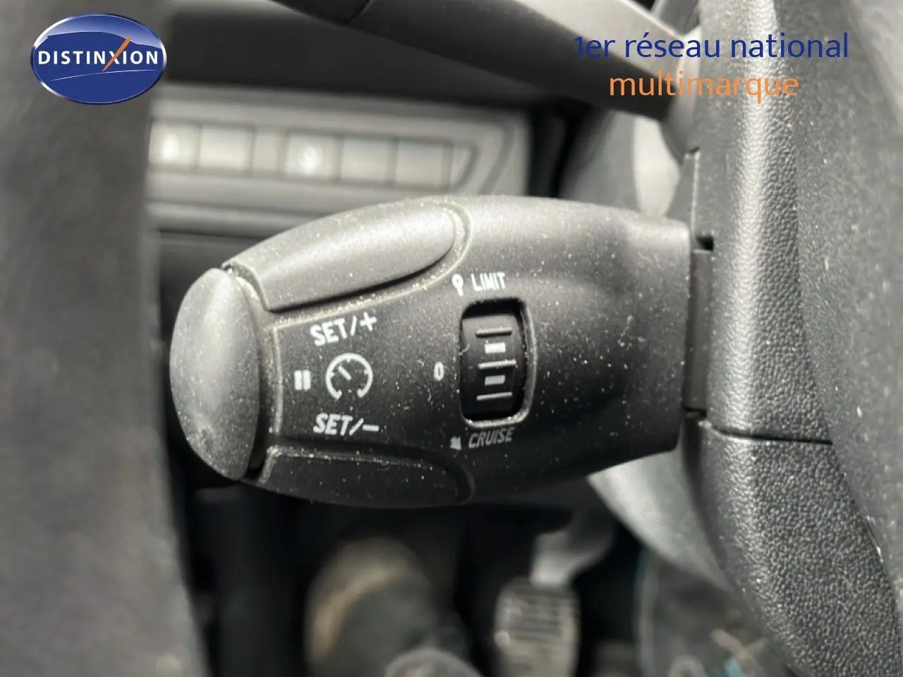 Gros plan sur la commande de régulateur de vitesse noire à gauche du volant d'une Peugeot 208 blanche banquise.