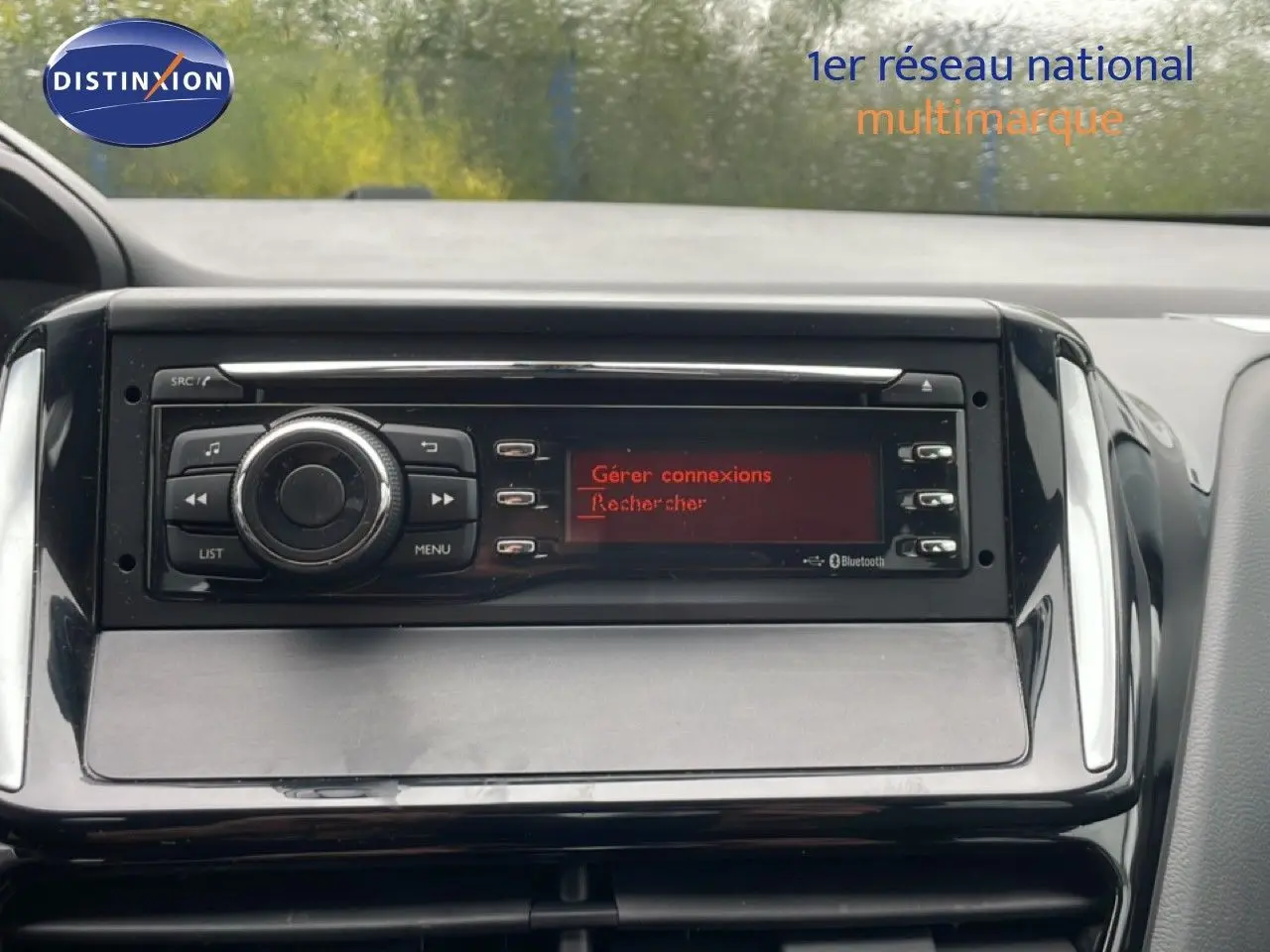 Vue rapprochée du tableau de bord de la Peugeot 208 Société blanche, mettant en valeur l’autoradio avec écran rouge et commandes.