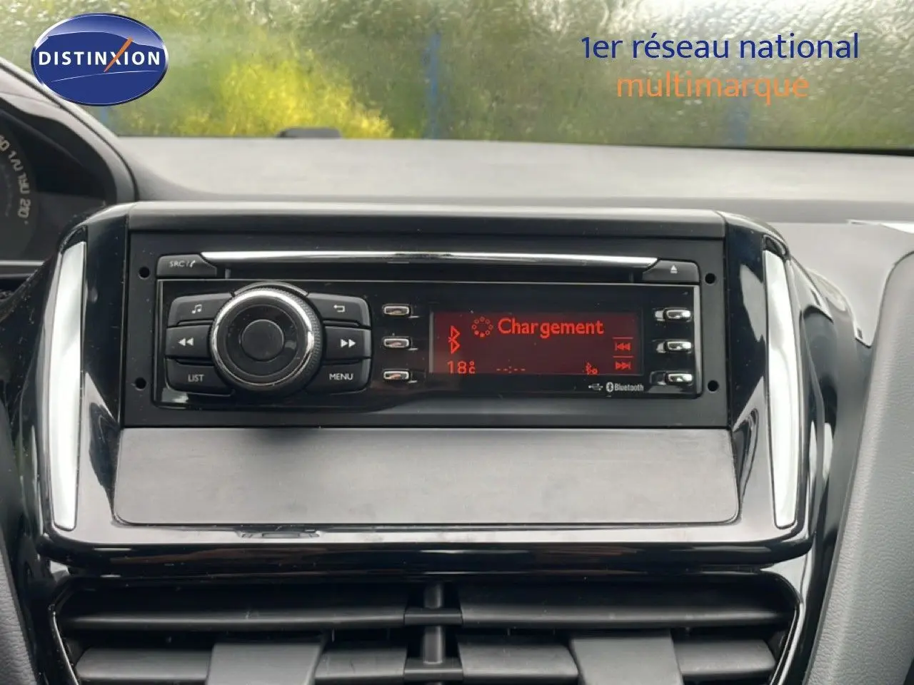 Gros plan sur la console centrale de la Peugeot 208 Société blanche, affichant l'autoradio avec écran rouge en mode Bluetooth.