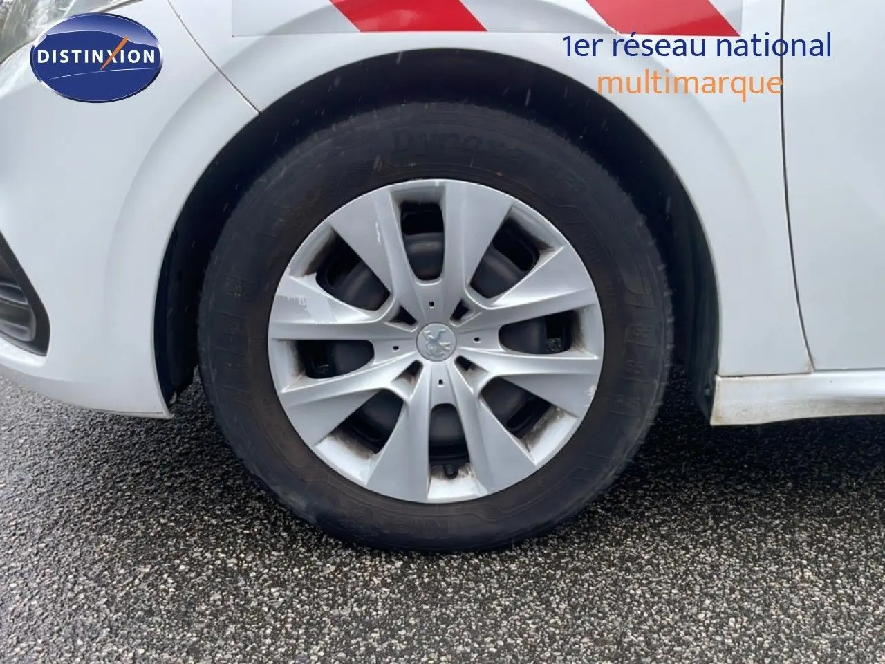 Gros plan sur la roue avant droite d'une Peugeot 208 Société blanche avec jante argentée et marquage rouge sur la carrosserie.