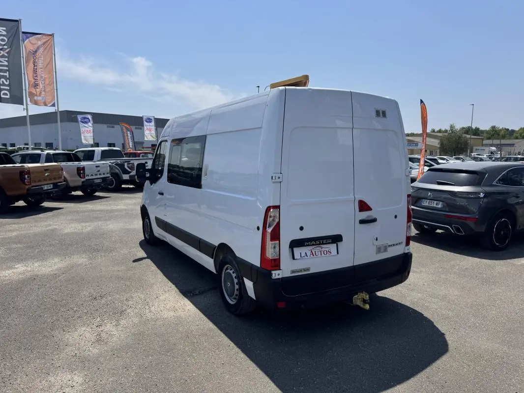 Renault Master blanc vue 3/4 arrière droit, fourgon utilitaire avec attelage et fenêtres latérales teintées.