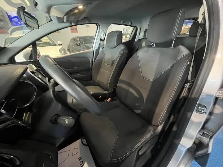 Vue intérieure côté conducteur de la Renault Clio IV gris argent, montrant les sièges noirs et le volant.