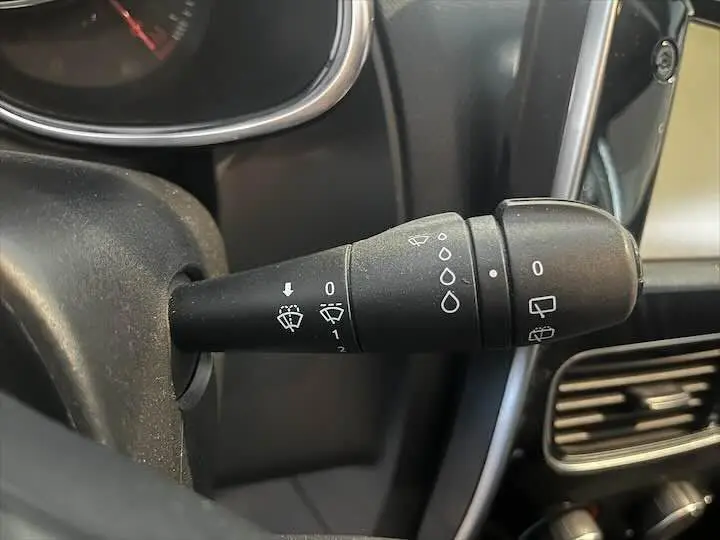 Gros plan sur la commande d'essuie-glace à gauche du volant dans l'habitacle noir d'une Renault Clio IV gris argent.