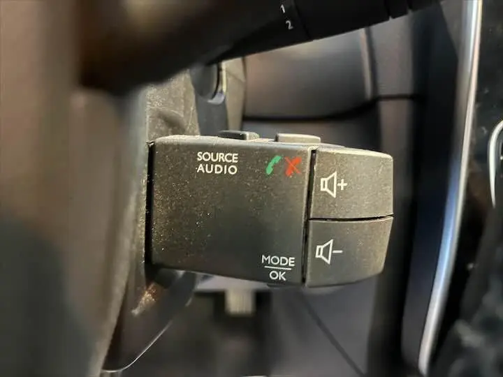 Gros plan sur les commandes audio au volant de la Renault Clio IV gris argent, avec boutons de volume et mode audio.