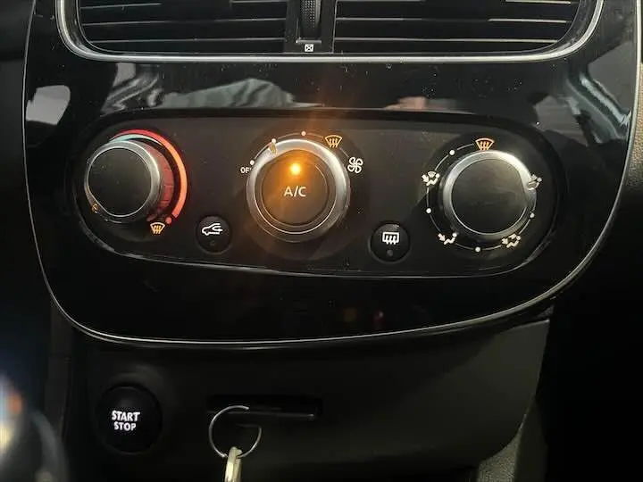 Gros plan sur les commandes de climatisation et bouton start/stop dans l'habitacle noir d'une Renault Clio IV gris argent.