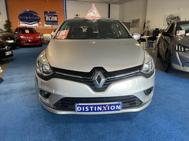 Vue frontale d'une Renault Clio IV gris argent exposée en showroom avec plaque Distinxion visible.