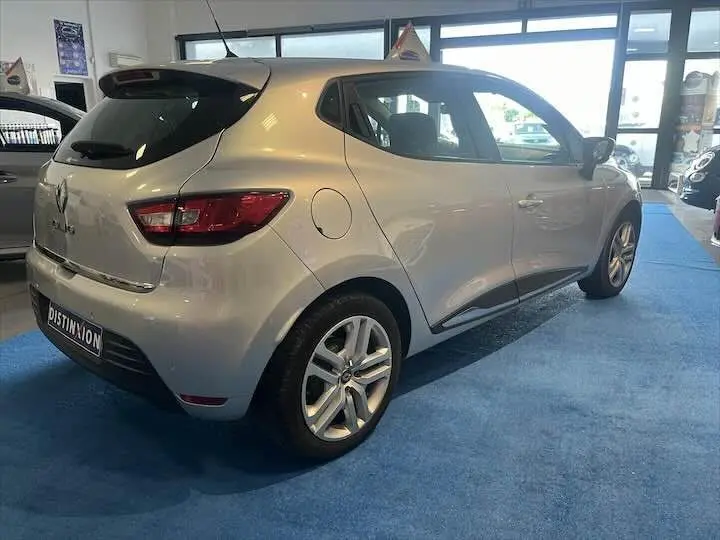 Renault Clio IV gris argent vue 3/4 arrière côté droit dans un showroom lumineux avec sol bleu.