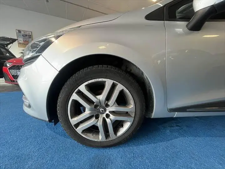 Gros plan sur la roue avant gauche d'une Renault Clio IV gris argent, avec partie avant et portière visibles.