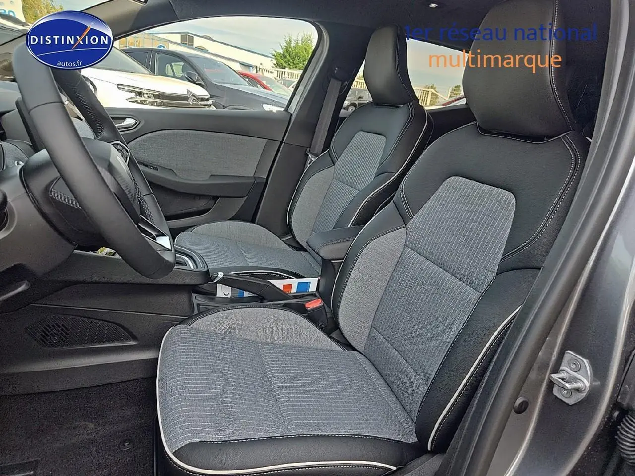 Intérieur avant côté droit de la Renault Clio V gris schiste, sièges tissu gris avec surpiqûres blanches visibles.
