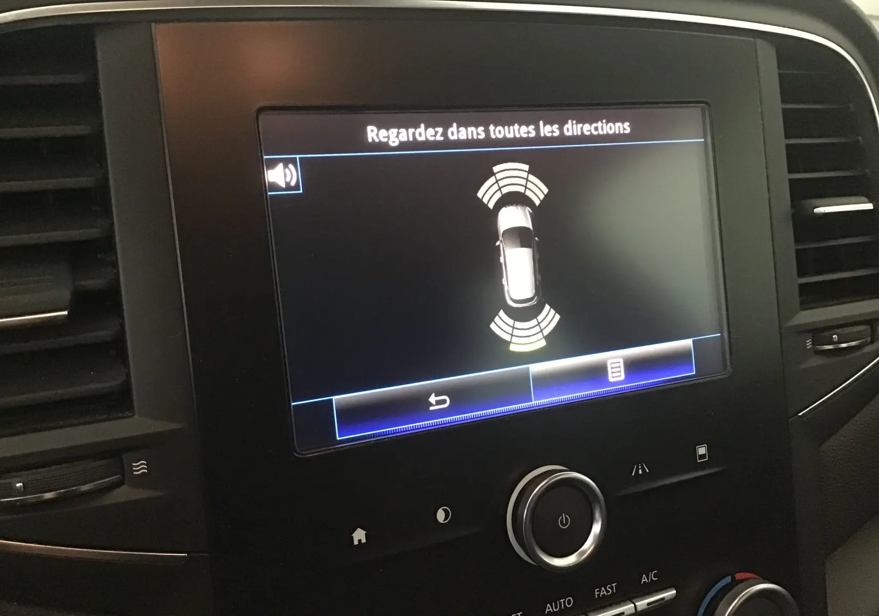 Écran central de la Renault Mégane IV Berline blanc montrant l'alerte de détection d'obstacles en mode stationnement.