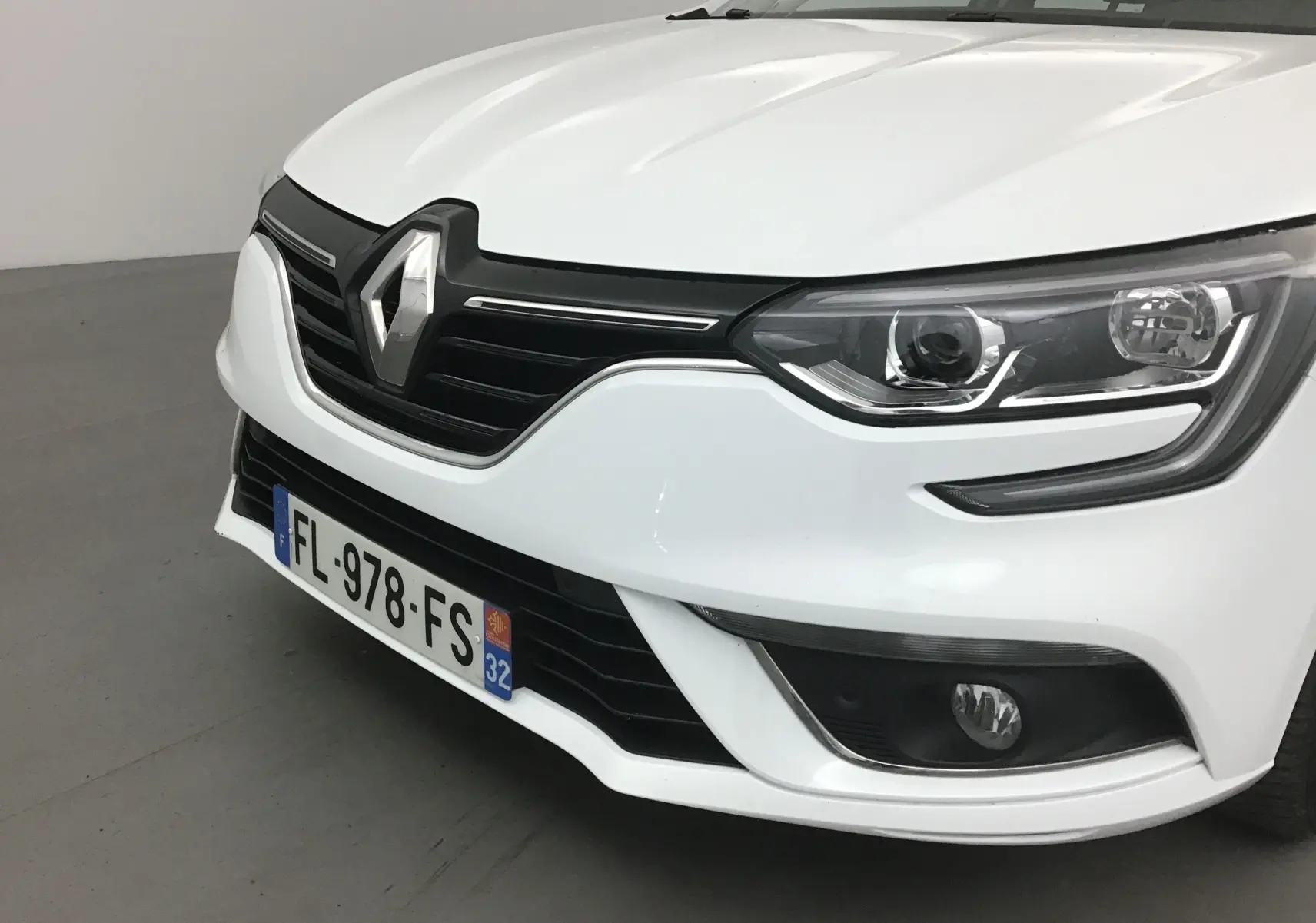 Vue avant droite d'une Renault Mégane IV Berline blanche de 2019 avec phares LED et calandre noire distinctive.