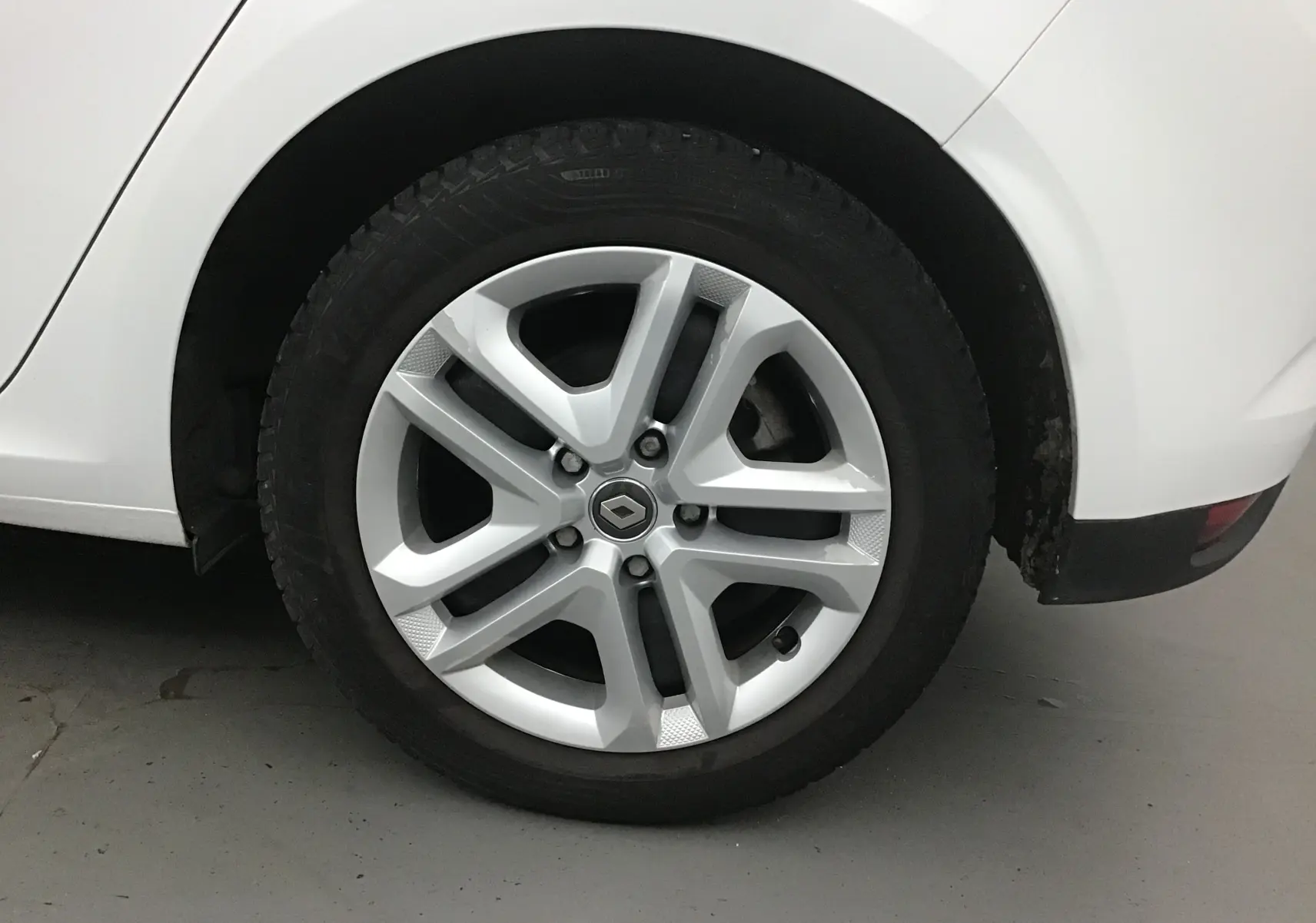 Gros plan sur la roue arrière droite blanche d'une Renault Mégane IV Berline 2019 avec jante alliage siglée Renault.