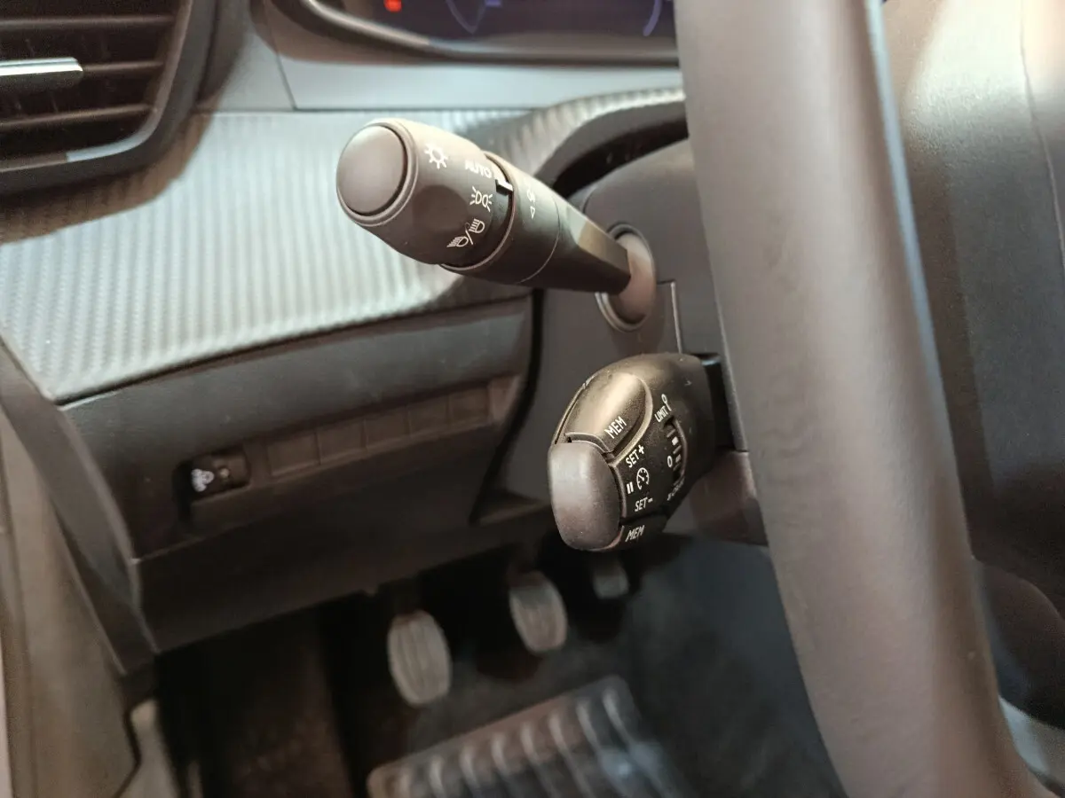 Gros plan sur les commandes au volant côté gauche du Peugeot 208 gris clair, avec levier de phares et régulateur de vitesse.