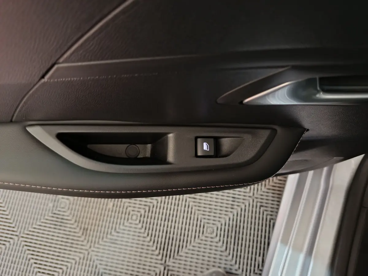 Poignée intérieure côté gauche de porte noire avec bouton de verrouillage éclairé sur Peugeot 208 gris clair 2025.