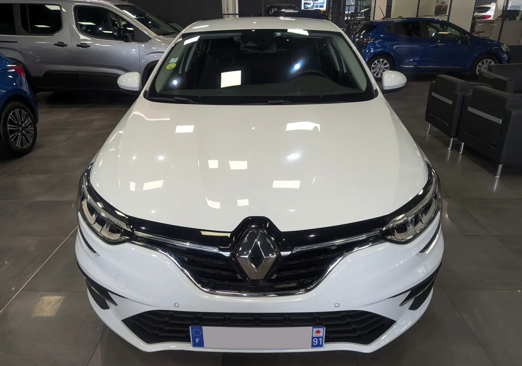Vue avant rapprochée d’une Renault Mégane IV Berline blanche Glacier, avec calandre noire brillante et logo Renault central.