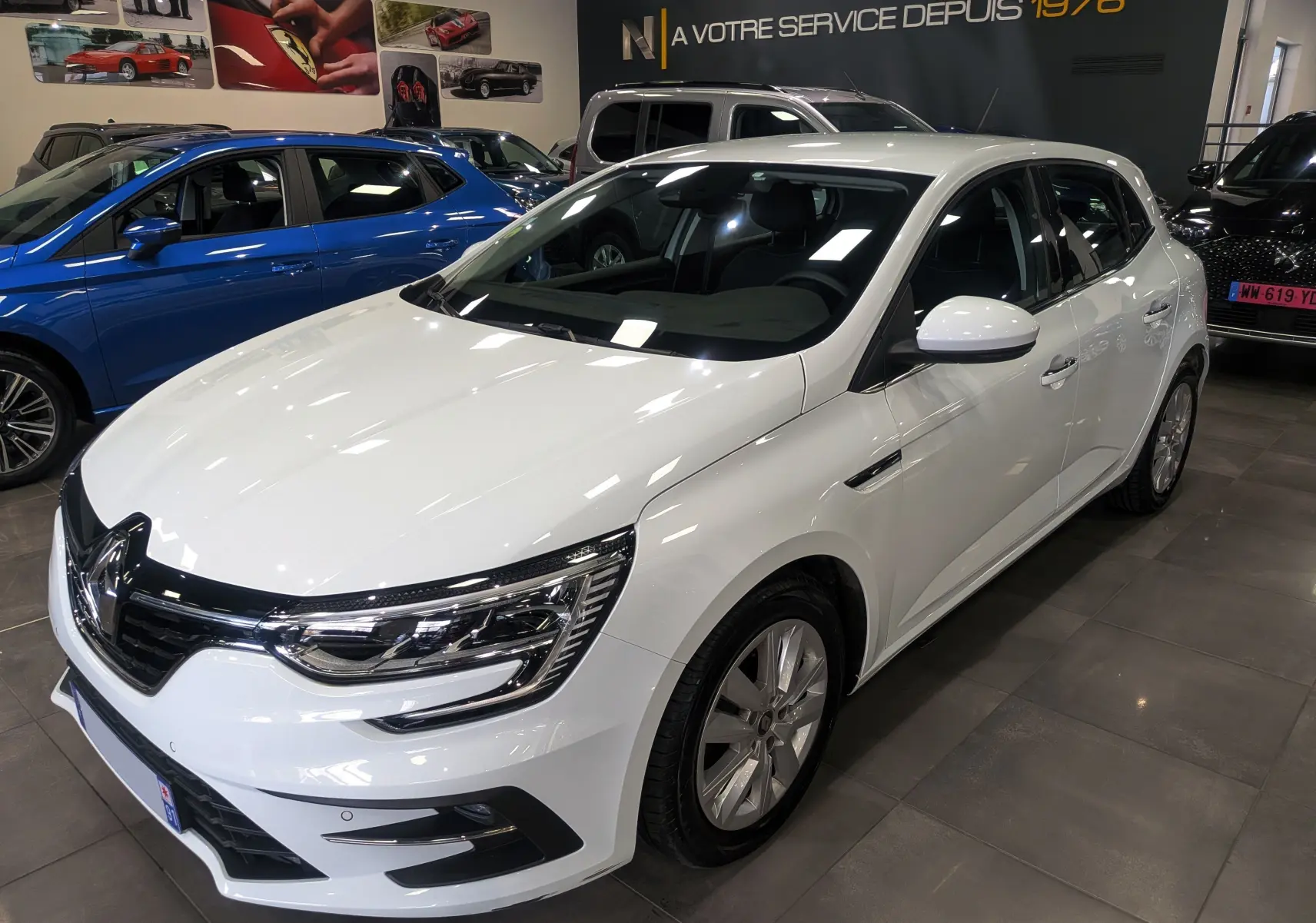 Vue 3/4 avant droite d'une Renault Mégane IV Berline blanche Glacier, avec phares LED et jantes alliage en concession.