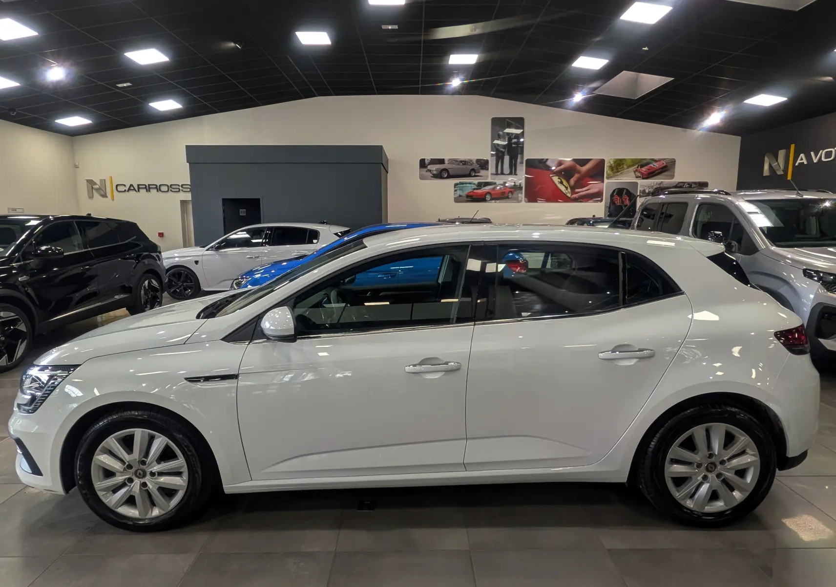Renault Mégane IV Berline blanc glacier vue de profil côté gauche dans un showroom lumineux avec jantes alliage.
