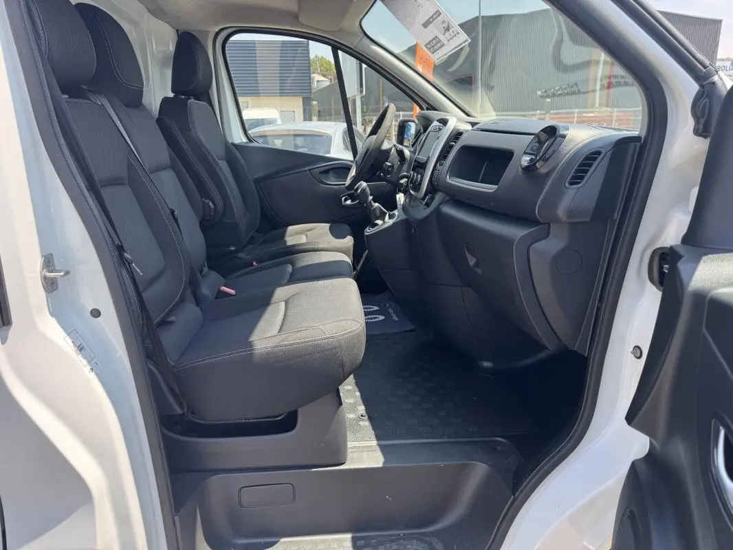 Intérieur du Renault Trafic Fourgon blanc 2019 vu côté droit, montrant les sièges avant et le tableau de bord noir.