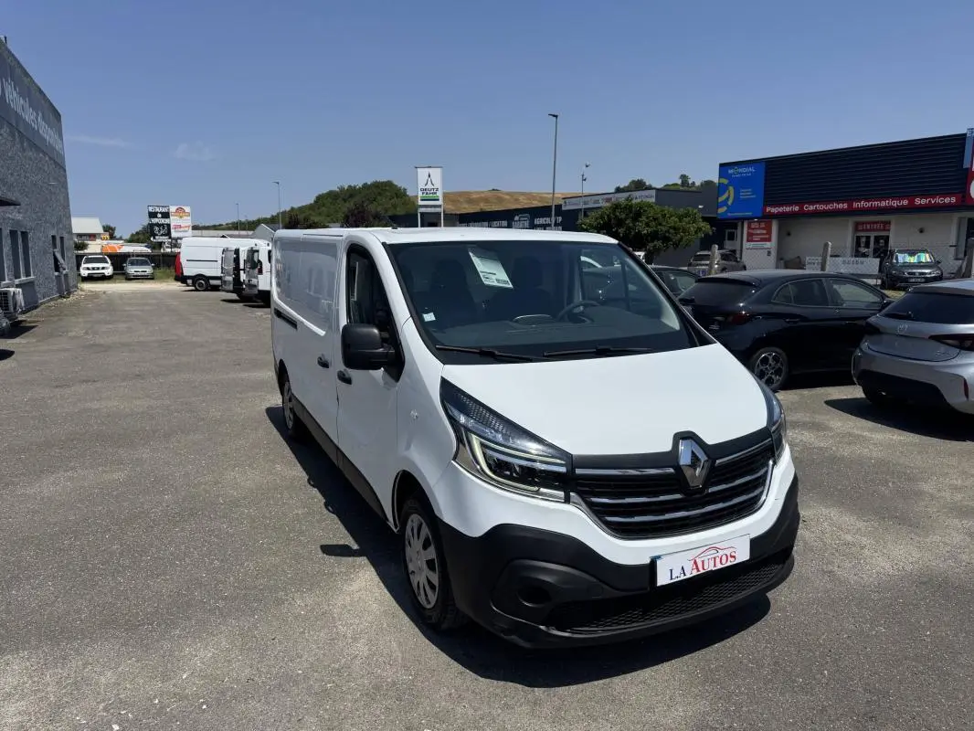 Renault Trafic Fourgon blanc vu en 3/4 avant droit sur un parking, avec calandre noire et phares modernes.