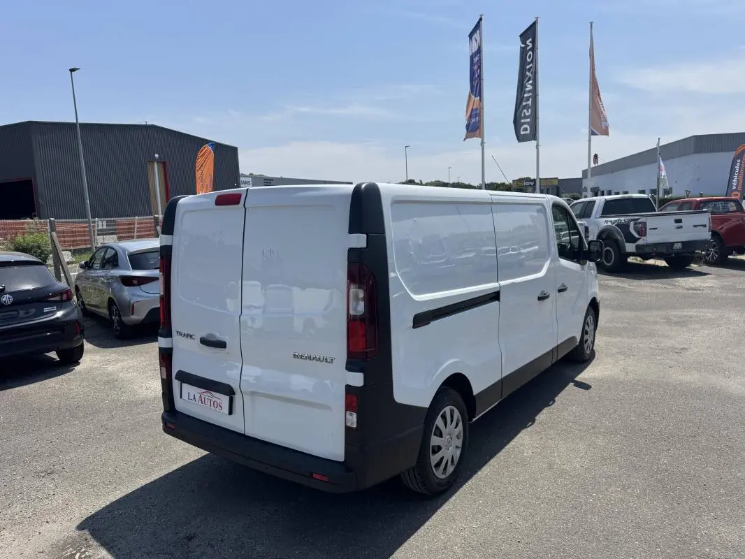 Vue 3/4 arrière droite d’un Renault Trafic Fourgon blanc stationné sur un parking extérieur.