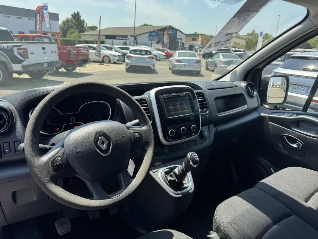 Intérieur du Renault Trafic Fourgon blanc 2019, vue côté conducteur montrant le volant, la console centrale avec écran tactile et levier de vitesses manuel.