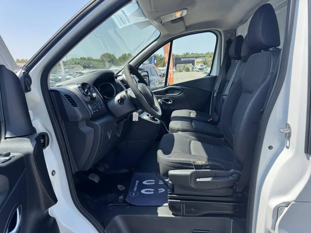 Vue intérieure côté conducteur du Renault Trafic Fourgon blanc 2019, montrant les sièges avant et le tableau de bord.