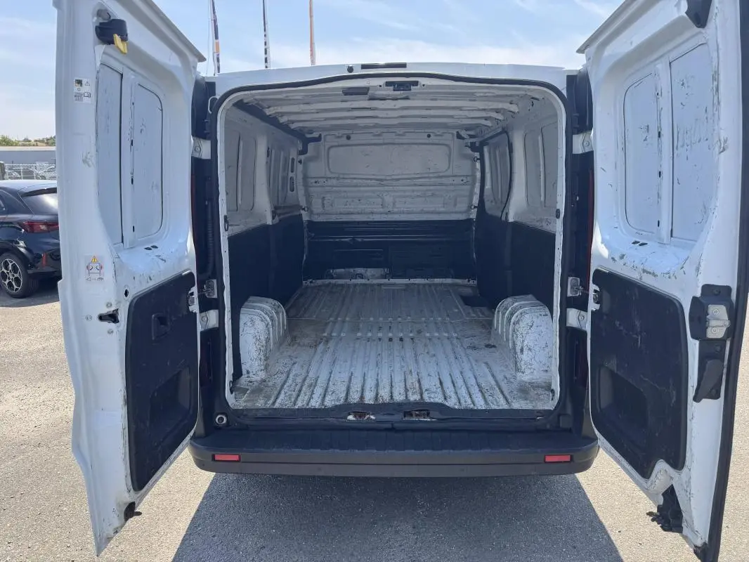 Vue arrière du Renault Trafic Fourgon blanc 2019 avec portes ouvertes montrant l’espace de chargement vide et usé.