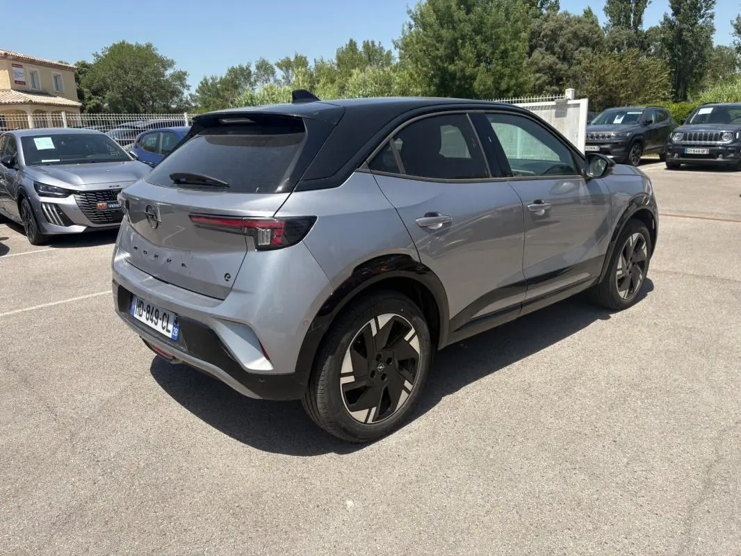 Opel Mokka électrique gris en 3/4 arrière droit, avec toit noir et jantes alliage 17 pouces, stationné en extérieur.