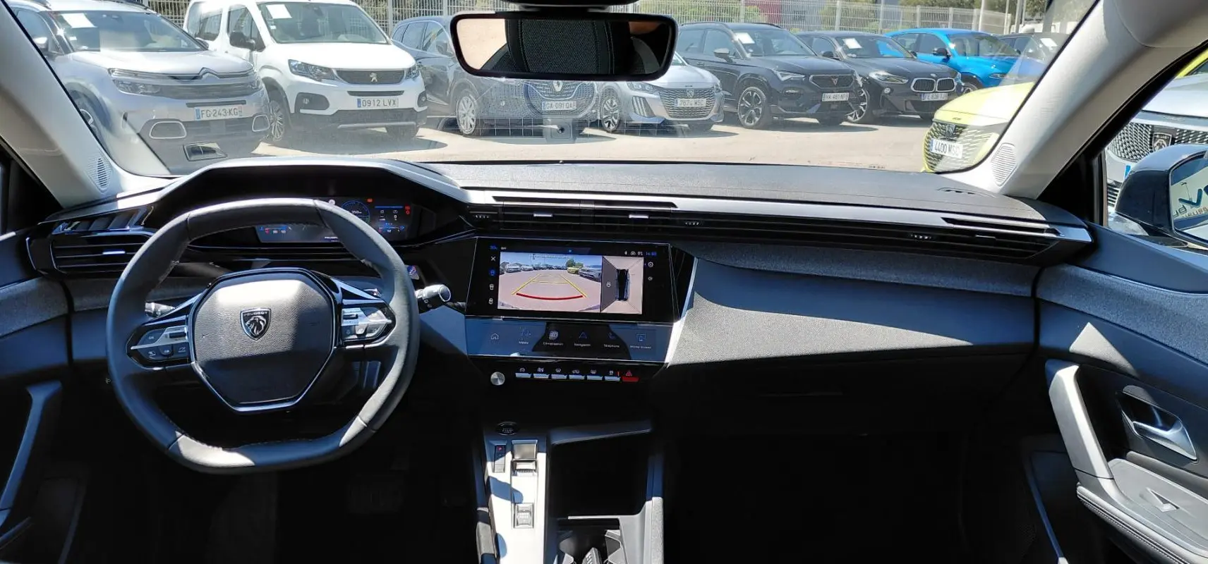 Vue intérieure frontale du tableau de bord de la Peugeot 308 SW Hybrid 145 gris, avec écran tactile affichant la caméra de recul.