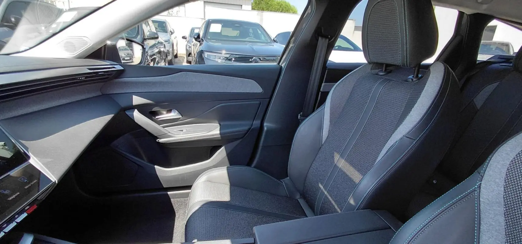 Vue intérieure côté passager avant d'une Peugeot 308 SW gris, mettant en valeur le siège tissu et cuir avec accoudoir central.