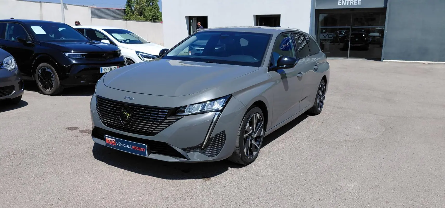 Peugeot 308 SW Hybrid gris vue 3/4 avant droit, avec calandre noire et jantes alliage 17 pouces visibles.