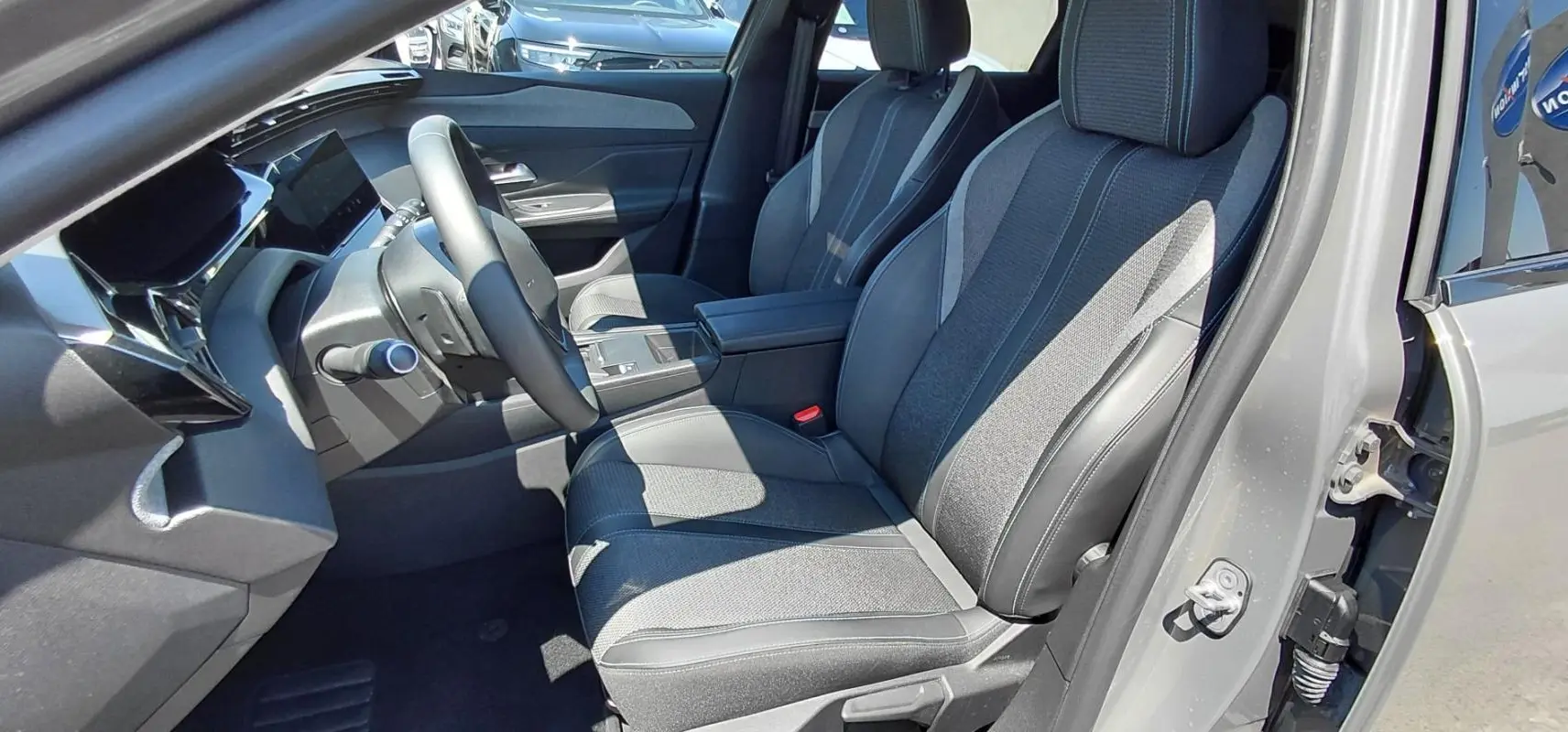 Vue intérieure côté conducteur du Peugeot 308 SW Hybrid gris 2025, montrant sièges tissu et cuir, volant et console centrale.