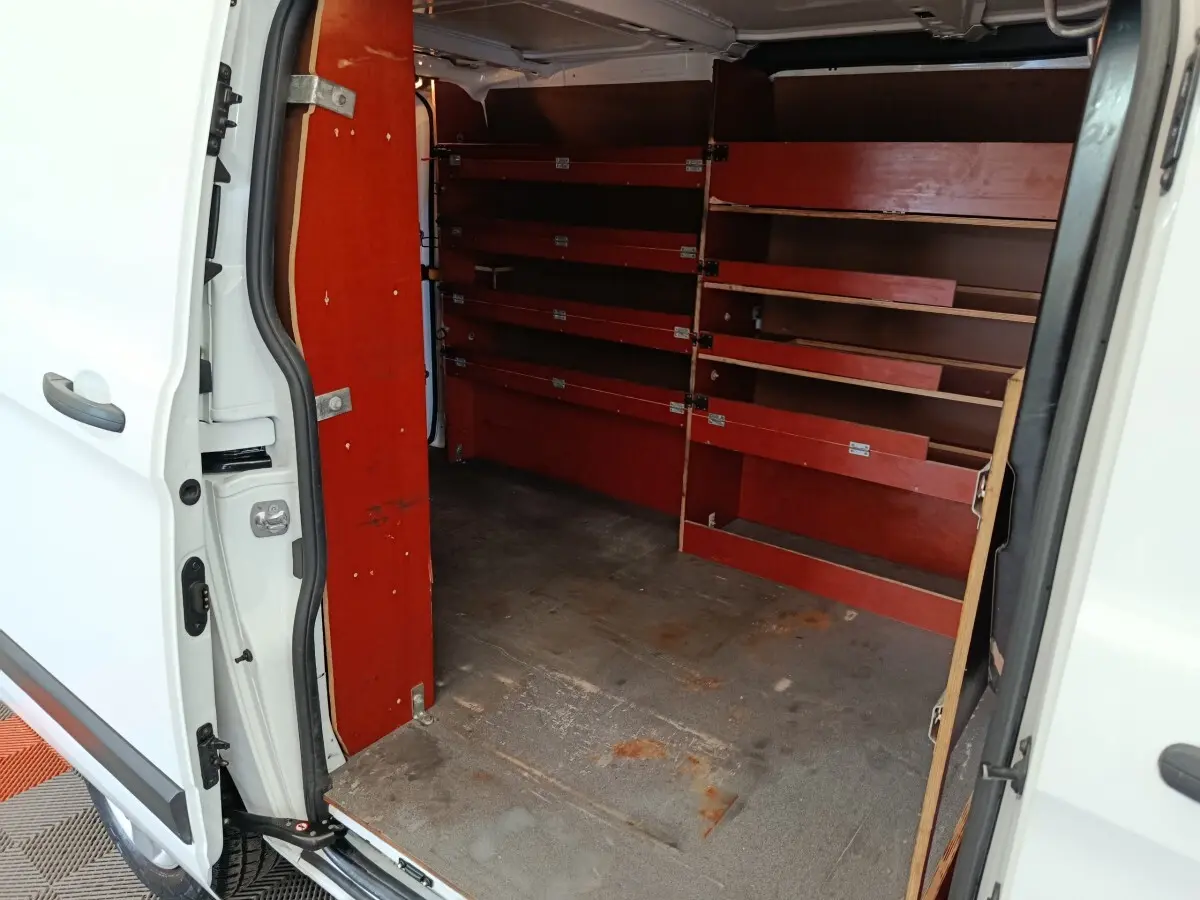 Vue intérieure côté droit du fourgon Ford Transit Custom blanc, montrant les étagères rouges de rangement.