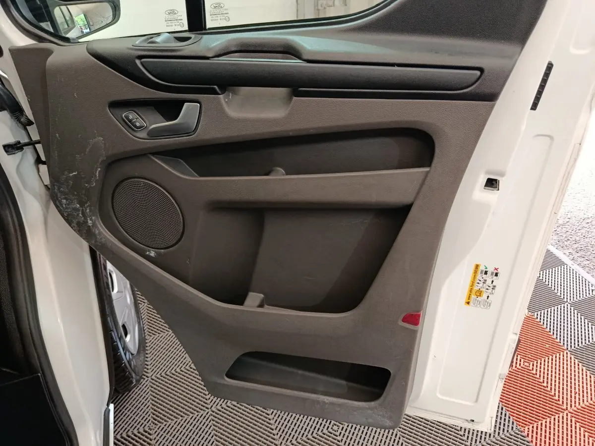 Vue intérieure côté gauche de la porte avant blanche du Ford Transit Custom Fourgon avec panneau noir et haut-parleur intégré.