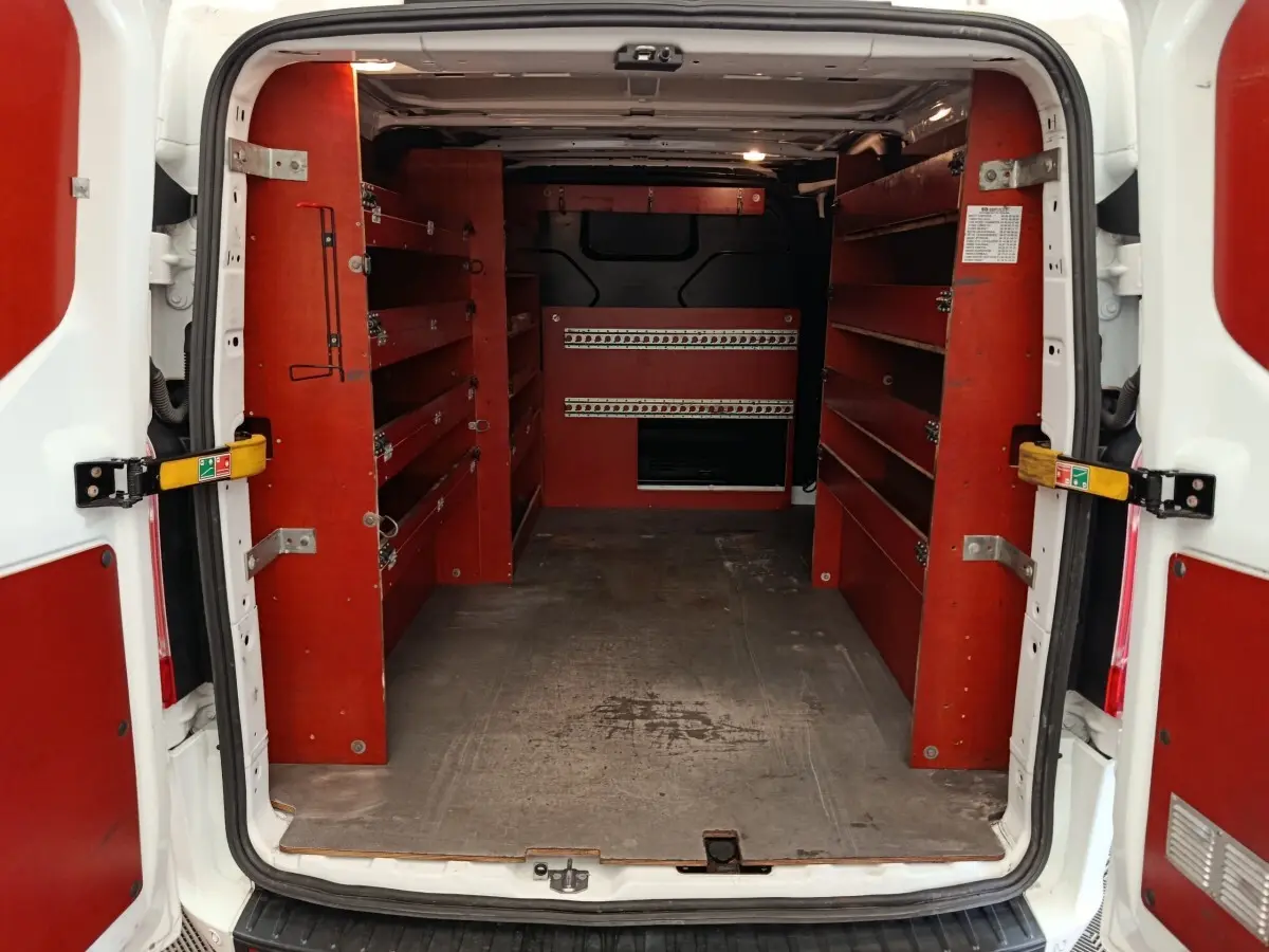 Vue arrière du Ford Transit Custom blanc de 2020, montrant l’intérieur utilitaire avec étagères rouges et cloison pleine noire.