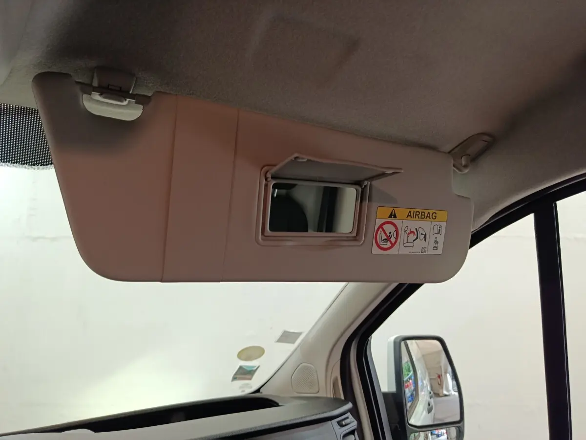 Vue intérieure côté conducteur du pare-soleil beige avec miroir et étiquette airbag dans un Ford Transit Custom blanc.