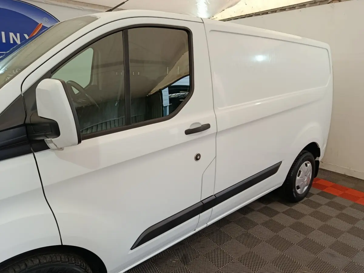 Vue latérale gauche d'un Ford Transit Custom blanc avec porte coulissante et rétroviseur blanc.