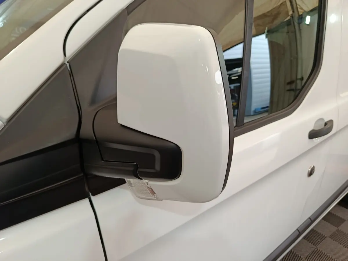 Gros plan sur le rétroviseur droit blanc du Ford Transit Custom Fourgon blanc, avec porte et poignée visibles en arrière-plan.