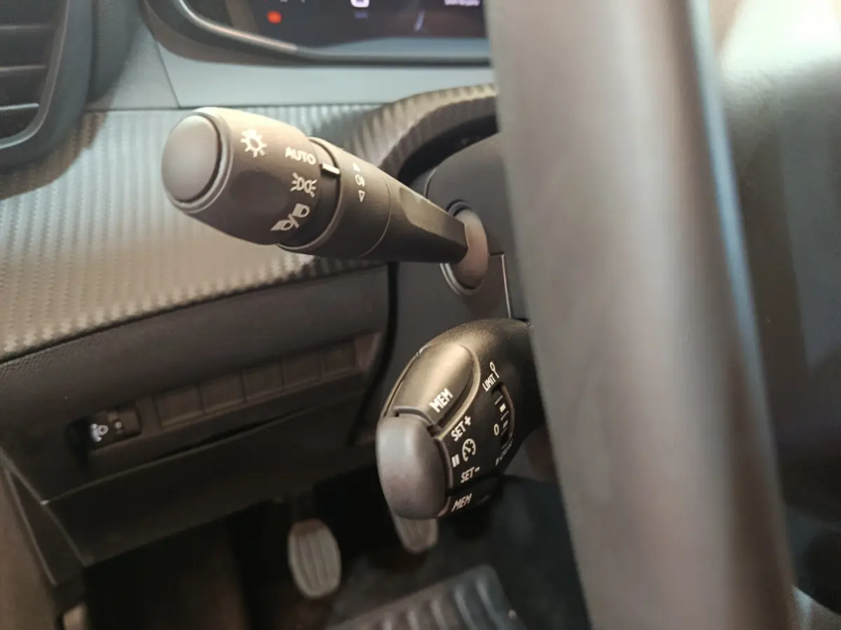 Gros plan sur les commandes au volant côté gauche du Peugeot 208 gris foncé, avec leviers de clignotant et régulateur de vitesse.