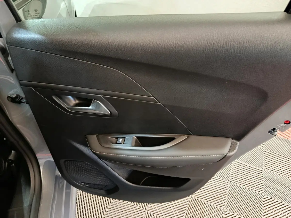 Vue intérieure côté gauche de la porte avant gris foncé de la Peugeot 208 PureTech 100 S&S Allure avec poignée et commande de vitre.