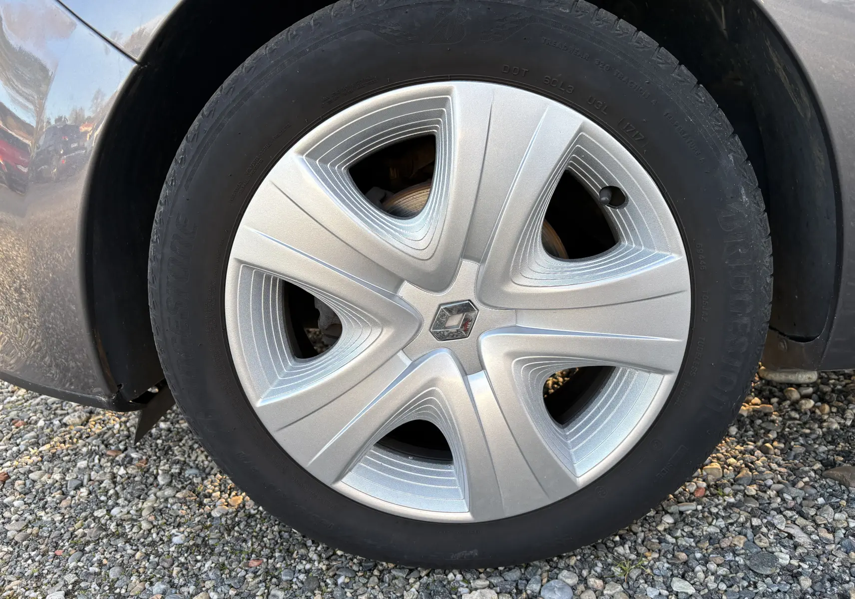 Vue rapprochée sur la roue arrière droite d'une Renault Clio IV gris métallisé garée sur un sol gravillonné.