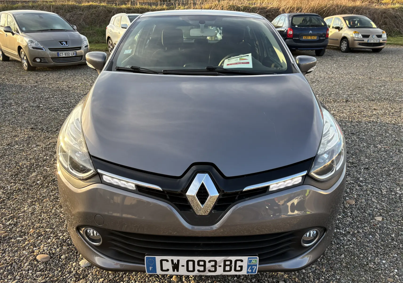 Vue avant d'une Renault Clio IV gris métallisé, mettant en valeur sa calandre noire et ses feux LED diurnes allumés.