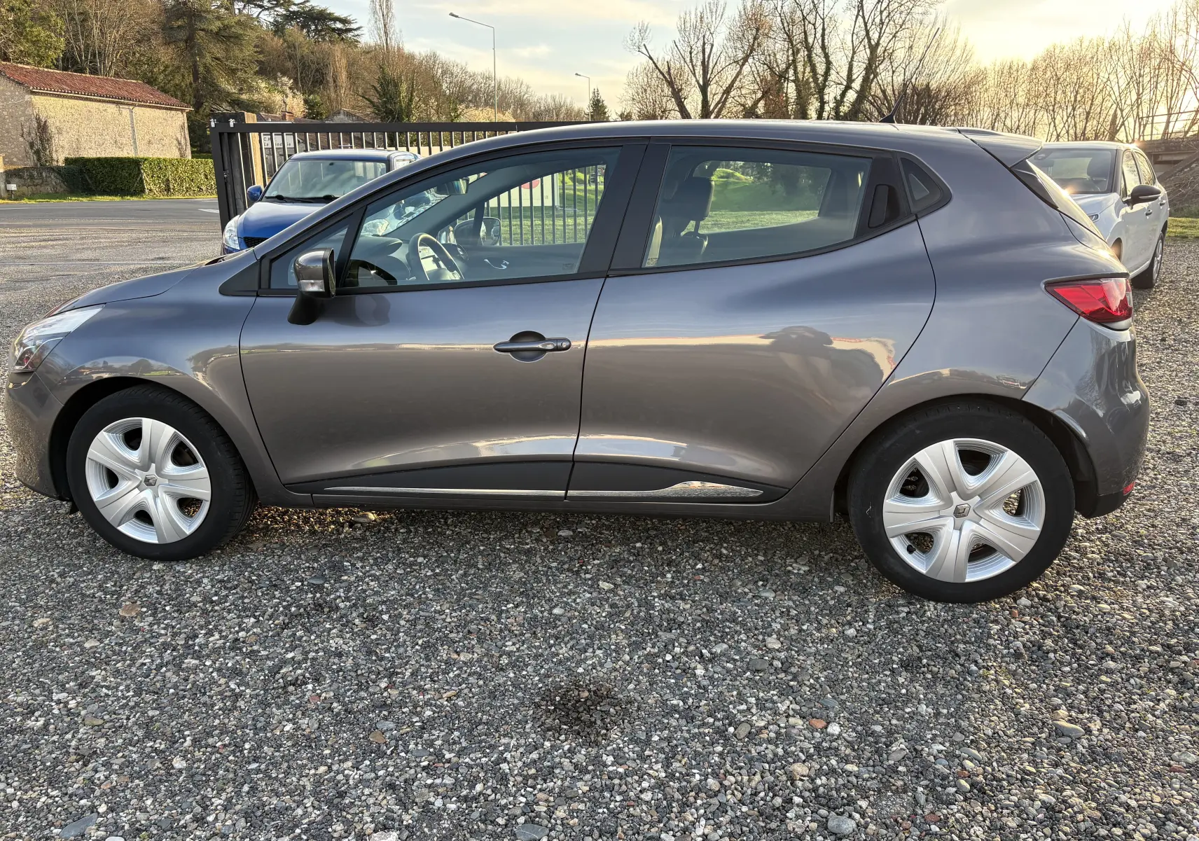 Profil côté gauche d'une Renault Clio IV gris métallisé de 2013, avec jantes et rétroviseur noir brillant.
