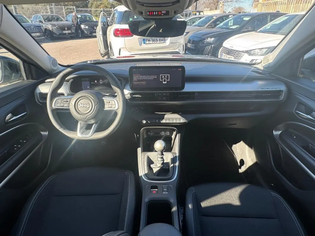 Vue intérieure avant du Jeep Avenger gris 2025, montrant le volant, tableau de bord digital et levier de vitesses manuel.