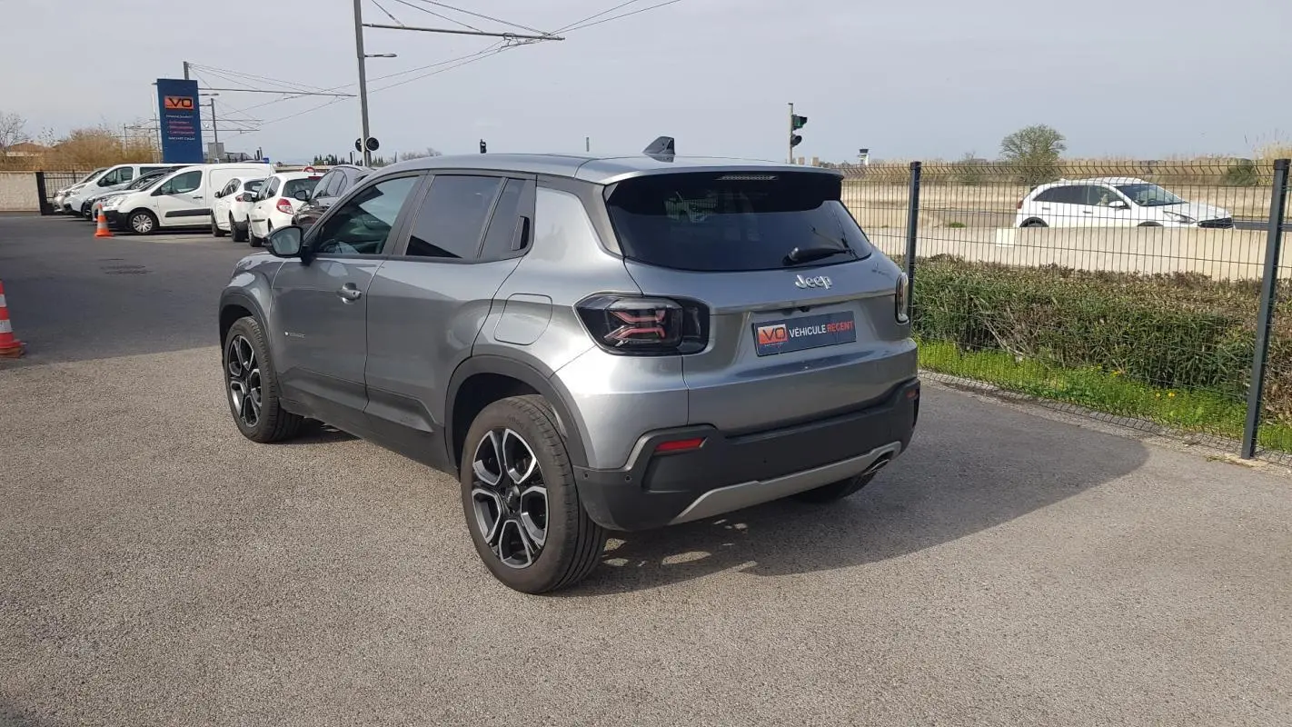 Vue 3/4 arrière gauche d’un Jeep Avenger gris métallisé avec jantes alliage 18 pouces, garé en extérieur.