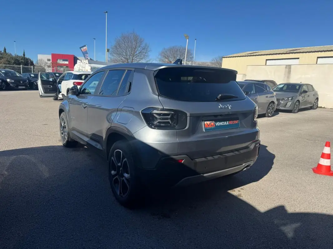 Jeep Avenger gris en 3/4 arrière droit, avec jantes alliage 18 pouces et feux arrière teintés, stationné en extérieur.