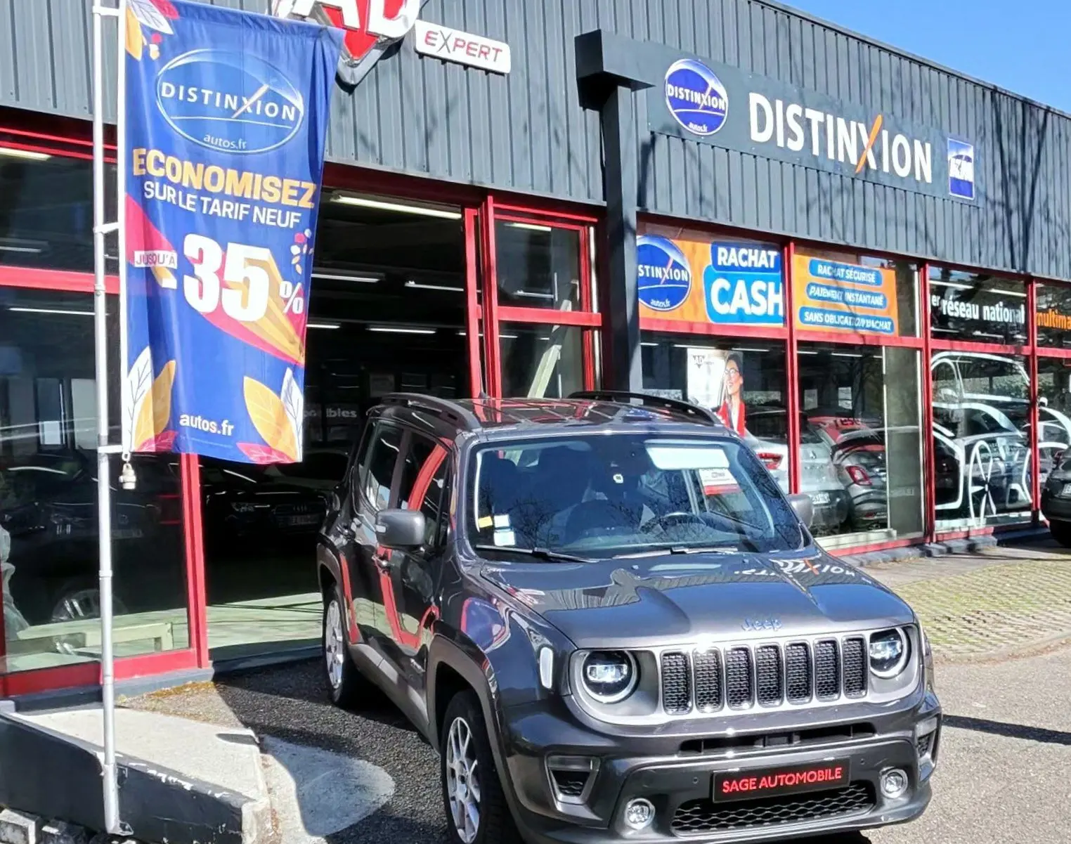 Jeep Renegade Granite Crystal métallisé en 3/4 avant droit, stationnée devant un garage avec enseignes commerciales.
